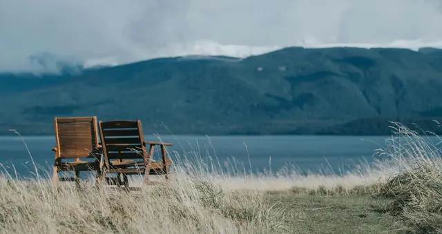 Two wooden armchairs looking out over calm water, representing collaborative Gottman Method couples therapy.